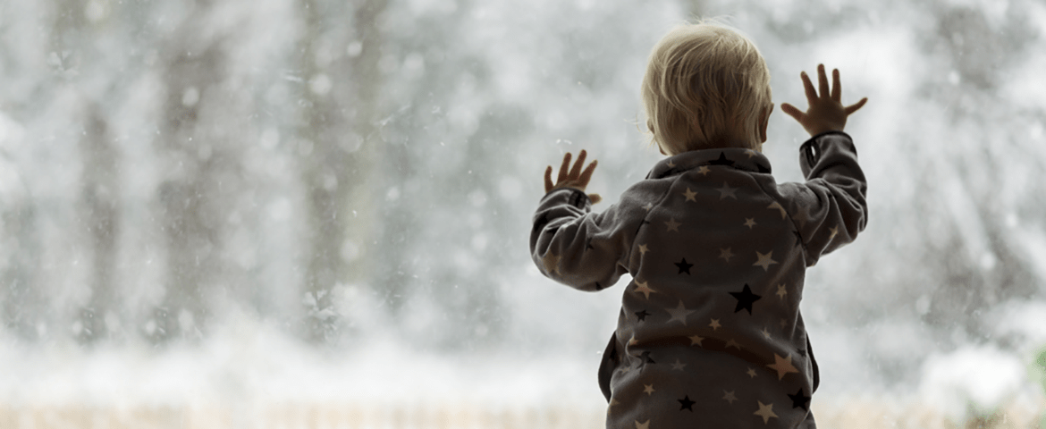 A child looking out the window at the snow