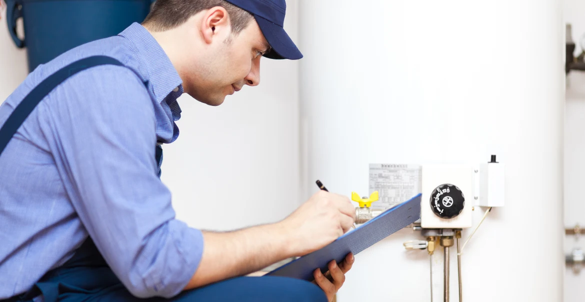 Technician taking notes on a clipboard while inspecting a water heater and its control components