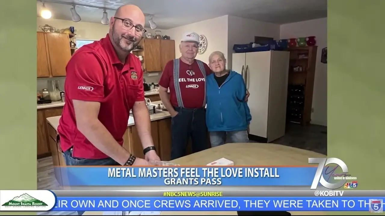 Two installers in red shirts standing inside a home with an older adult, with an HVAC unit visible nearby.
