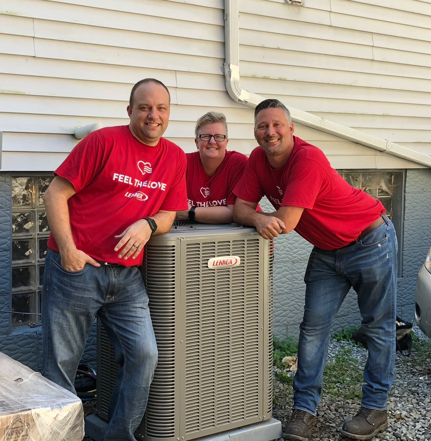 Three people in red shirts leaning over a Lennox AC